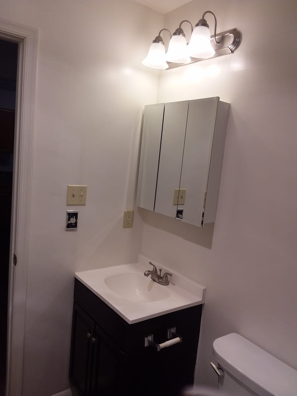 A bathroom at Indian Head Elderly Apartments with a white sink set in a dark vanity, a mirrored medicine cabinet, and a three-light fixture above