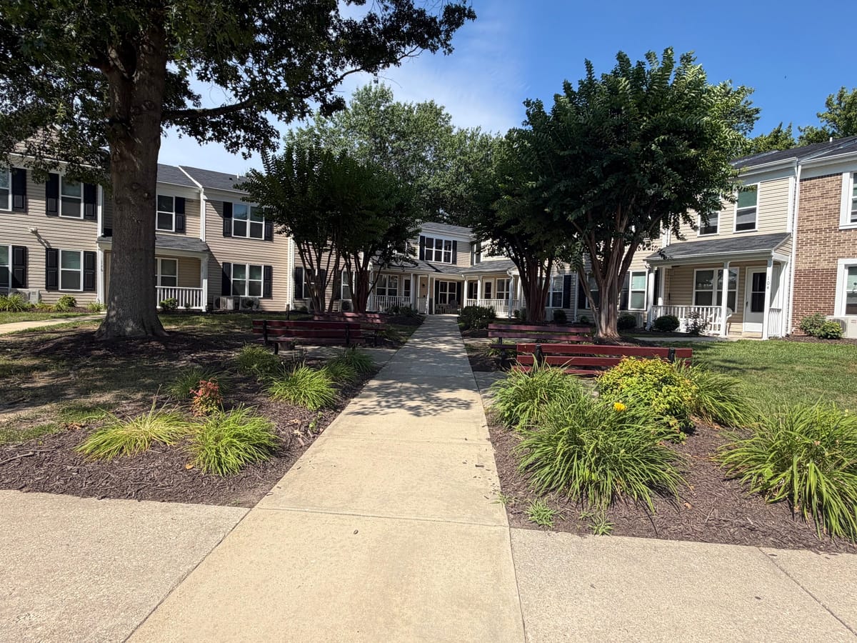 The central walkway through the courtyard at Indian Head Elderly Apartments, lined with planted beds and red benches and leading to a covered entrance