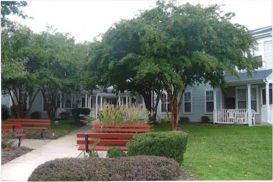 A landscaped courtyard at Indian Head Elderly Apartments with red benches and a walkway among crepe myrtle trees