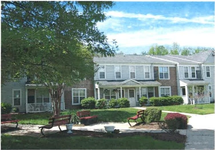 Two-story Indian Head Elderly apartment homes with light siding and brick, benches along a sunny walkway