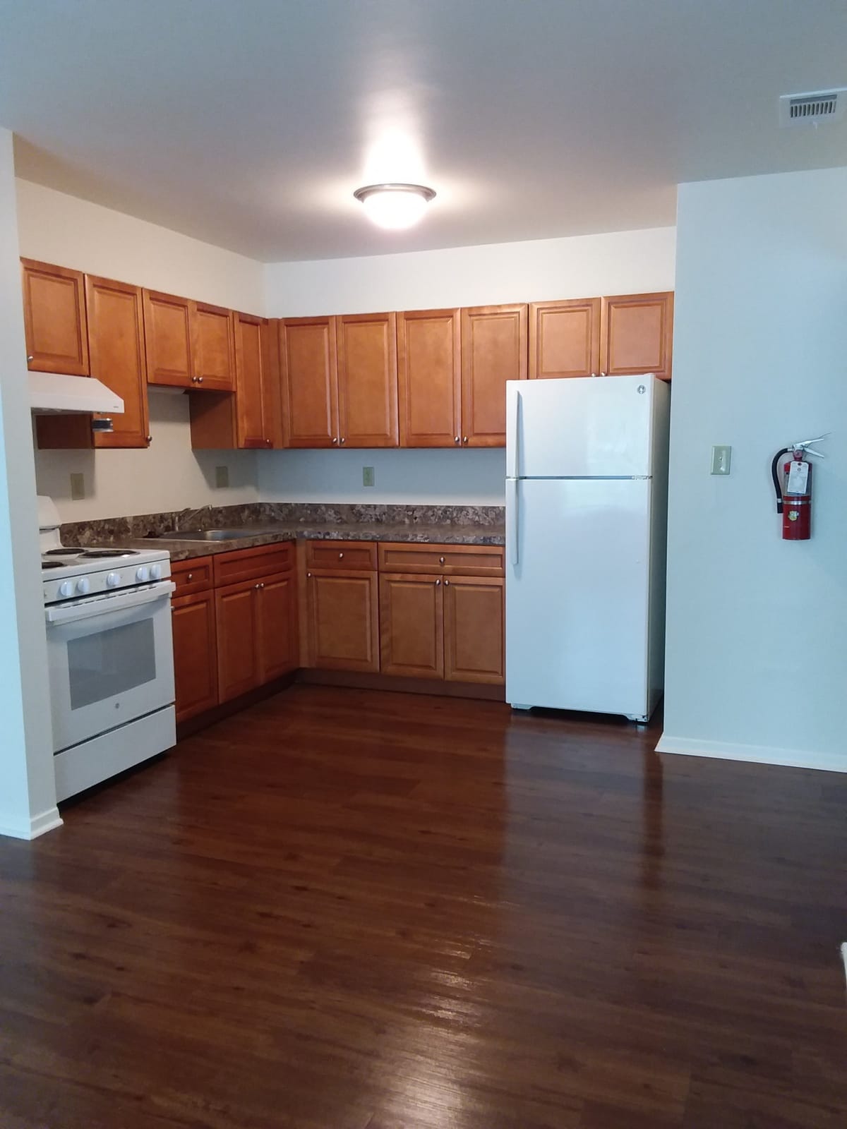 A kitchen at Indian Head Elderly Apartments with wood cabinets, a white range and refrigerator, a stainless sink, and wood-look plank flooring