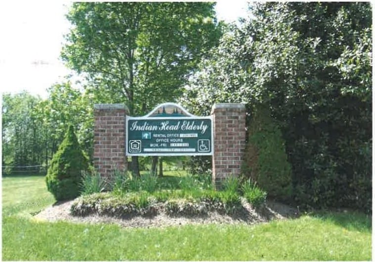 The Indian Head Elderly entrance sign on brick pillars, surrounded by green shrubs and trees